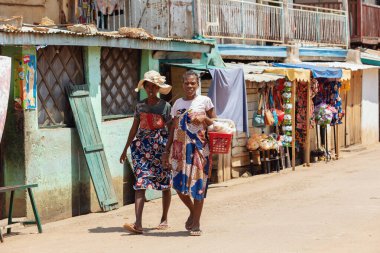 Miandrivazo, Madagascar - October 11 2025: Two Malagasy women in traditional lamba walking through a busy market street in Miandrivazo, Menabe.
