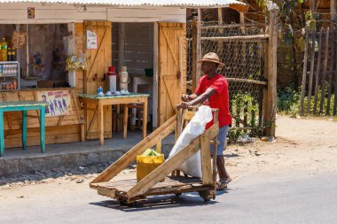 Mahavory, Toamasina Eyaleti, Madagaskar - 17 Ekim 2016: Bir adam, yerel ticaret ve taşımacılık yöntemlerini vurgulayarak, küçük bir ahşap dükkandan geçen tahtadan bir el arabasını itti.