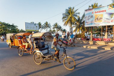 Toamasina, Madagaskar - 21 Ekim 2025: Tamatave 'de trafik ve sokak hayatı, reklam panoları ve hindistan cevizi satıcılarının önünden geçen yerel siklon ve tuk-tuk taşımacılığı.