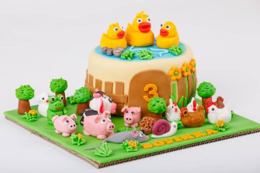 Üç yaşındaki bir doğum günü pastasının yakın çekimi. Pastanın tepesinde havuzda lastik ördekler var. İnekler, domuzlar ve tavuklar hayvan çiftliğine benziyor..