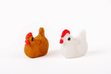 İki el yapımı badem ezmesi tavuk heykelciği, biri beyaz, biri kahverengi, beyaz arka planda izole edilmiş..