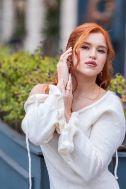 Açık havada yüzlerine dokunan beyaz elbiseli kızıl saçlı kadının moda portresi.