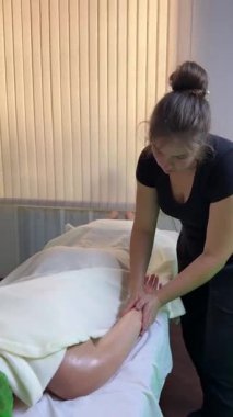 Masaj terapisti, masaj sırasında, yeşil havlu ve beyaz çarşafla, spa odasına baskı uyguluyor.