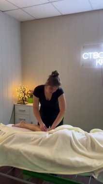 Kadın masaj terapisti spa salonunda profesyonel bacak masajı yapıyor. Modern iç mekânda masaj masasında sakin bir sağlık terapisi.