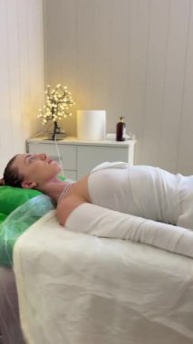 Spa salonunda tam vücut sıkıştırma seansı, masaj masasında uzanan genç bir kadın, rahatlatıcı cilt bakımı ve vücut şekillendirme için tedavi sırasında.