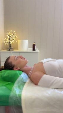 Spa salonunda tam vücut sıkıştırma prosedürü, masaj masasında uzanan genç bir kadın rahatlatıcı vücut şekillendirme ve cilt bakımı sırasında