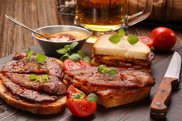 Сэндвич с жареным беконом и пивом на деревянном фоне — стоковое фото
