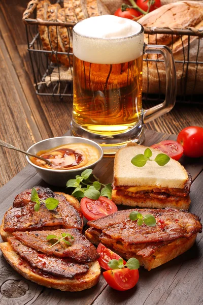 Σάντουιτς με τηγανητό μπέικον και μπύρα σε ξύλινο φόντο — Φωτογραφία Αρχείου