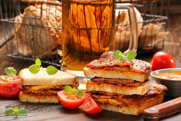 Sandwich with fried bacon and beer on wooden background — Stock Photo, Image