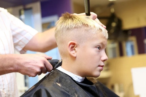 Hairdresser trimming blonde hair of young boy by scissors — Stock Photo, Image