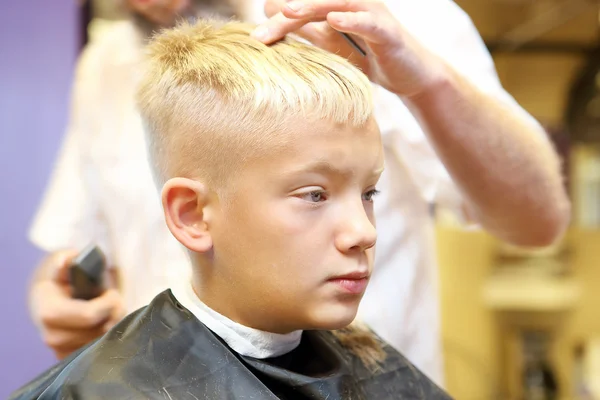 Barber cutting hair of young boy by electric trimmer — Stock Photo, Image