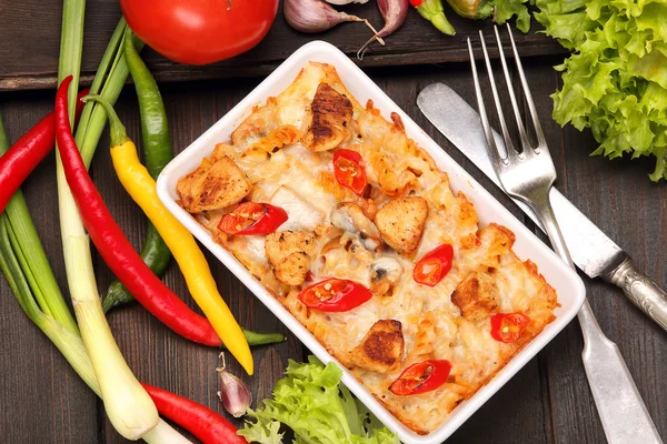 Casserole with chicken and chili peppers on a wooden background — Stock Photo, Image