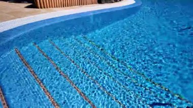 Güneşli bir günde, açık mavi su ve merdivenleri olan lüks bir tatil köyünde ya da otelde yüzme havuzu.