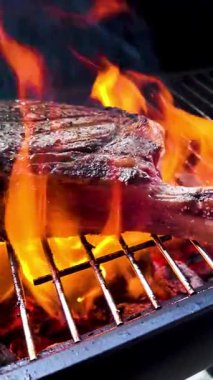 Ağır çekimde alevlerle ızgarada baltalı bifteğin dikey görüntüsü.