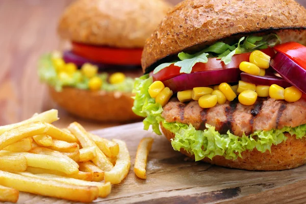 Hamburguesa a la parrilla con papas fritas, tomate, cebolla y maíz en madera b —  Fotos de Stock