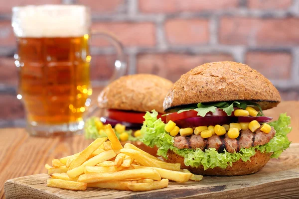 Hamburguesa a la parrilla con papas fritas y cerveza sobre fondo de pared de ladrillo —  Fotos de Stock