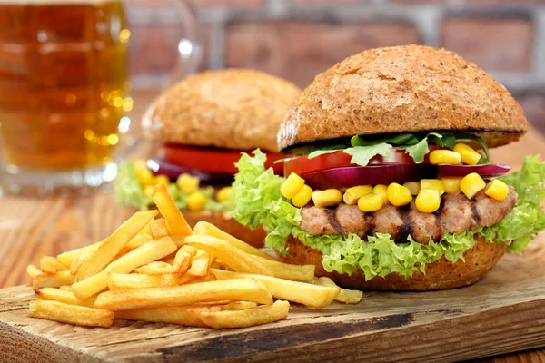 Grilovaný hamburger s hranolky, rajčaty, cibulí a kukuřice na dřevěné b — Stock fotografie