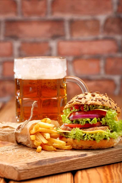Grilovaný hamburger s hranolky a pivo na cihlovou zeď pozadí — Stock fotografie