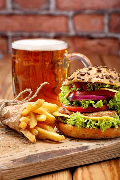 Grilovaný hamburger s hranolky a pivo na cihlovou zeď pozadí — Stock fotografie