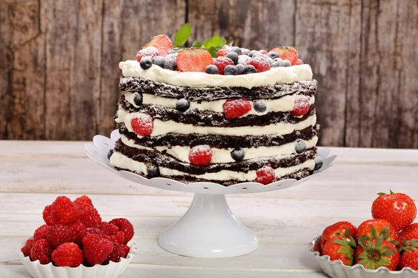 Gâteau au chocolat avec crème blanche et fruits frais sur fond en bois — Photo