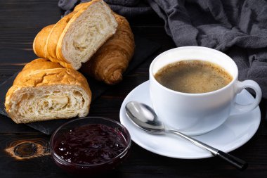 Reçelli taze kruvasan ve koyu arkaplanda kahve. Fransız kahvaltısı. 