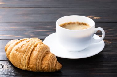 Tahta masada bir fincan kahve ve kruvasan. Üst görünüm.