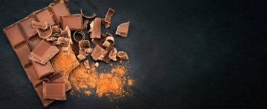 Kırık çikolata parçaları ve siyah bir arka planda kakao tozu. Uzayı kopyala. Pankart.