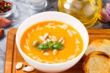 Balkabağı ve havuç çorbası kremalı ve kabak tohumlu ahşap arka planda.