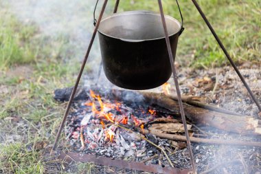 Ateşin üzerinde asılı duran bir turist potası. Kampanyada yemek pişirme.