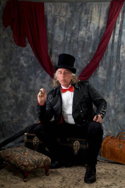 Victoria Steampunk 'ın portresi, izleyiciye bakıyor, silindir şapka, kuyruk palto giyiyor, papyon takıyor ve bagajda oturuyor..
