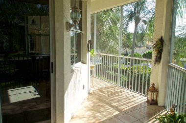 Florida 'da yüksek katlı bir apartmanın balkonunda ikinci kattaki balkonda arka planda palmiye ağaçları ve binalar bulunan verandanın dış kapısı ve penceresi görülüyor.
