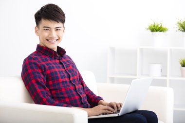 mutlu genç adam dizüstü bilgisayar ile kanepede rahatlatıcı