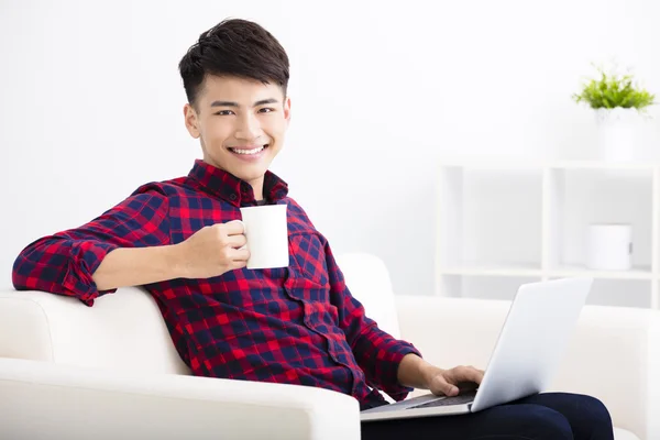 Jovem feliz relaxando no sofá com laptop — Fotografia de Stock