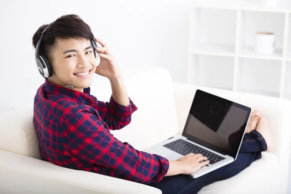 Jovem bonito usando computador portátil com fone de ouvido — Fotografia de Stock