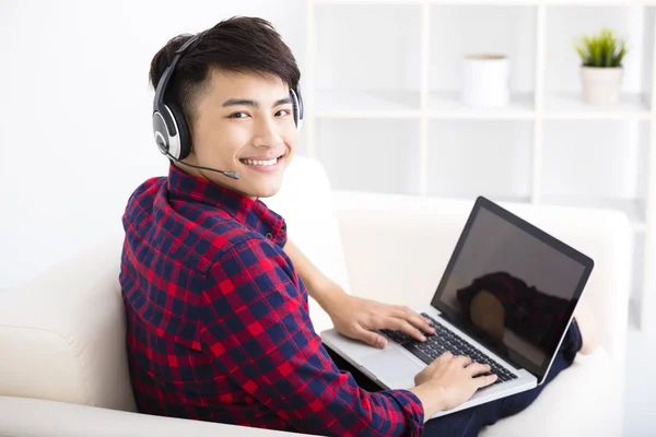 Joven guapo usando ordenador portátil con auriculares — Foto de Stock