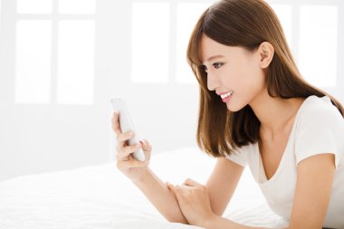 Genç gülümsemek kadın yatakta akıllı telefon okuma