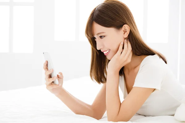 Jovem sorrir mulher ler telefone inteligente na cama — Fotografia de Stock