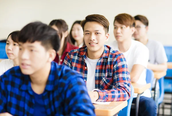 Улыбающийся студент колледжа, сидящий с одноклассниками — стоковое фото