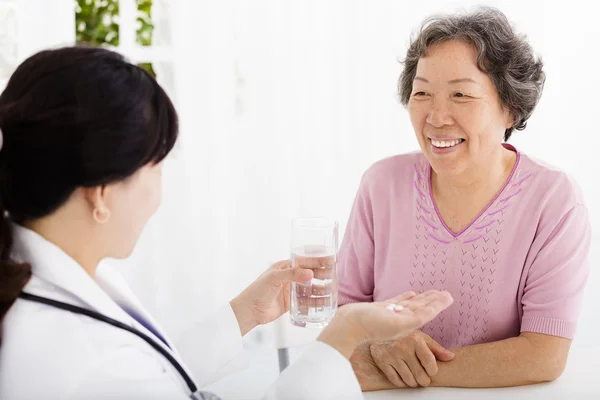 Arzt gibt Seniorin Medikamente und Wasser — Stockfoto