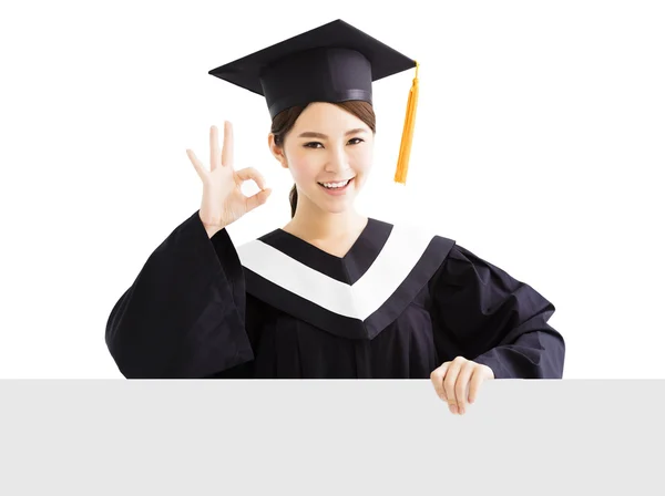 Feliz graduado feminino mostrando placa em branco com gesto ok — Fotografia de Stock