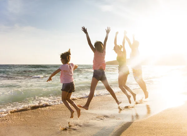 Happy young family jumping on beach at sunset — Stock Photo, Image