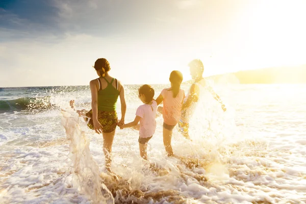 Glückliche junge Familie spielt am Strand bei Sonnenuntergang — Stockfoto