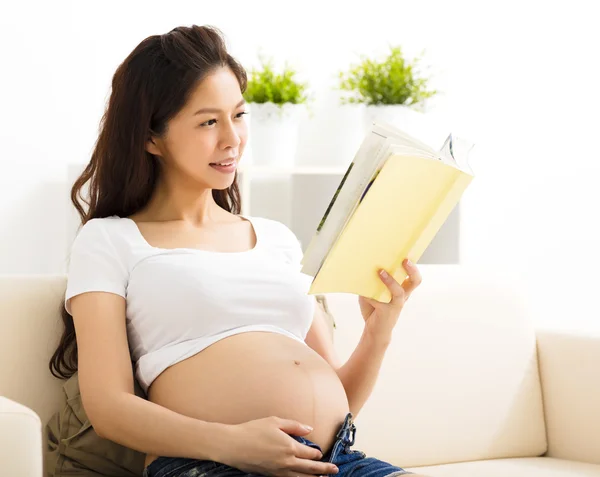 Беременная женщина отдыхает дома и читает книгу на диване — стоковое фото