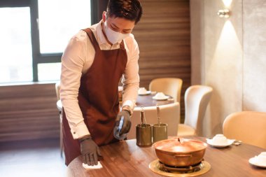 Restoranda dezenfekte ederken koruyucu yüz maskesi takan garson.