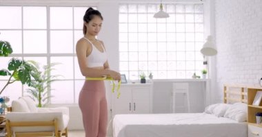 Mutlu genç bir kadın ölçü bandıyla belini ölçüyor.