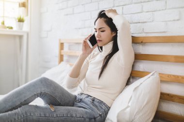 Evde cep telefonuyla konuşan mutsuz genç bir kadın.