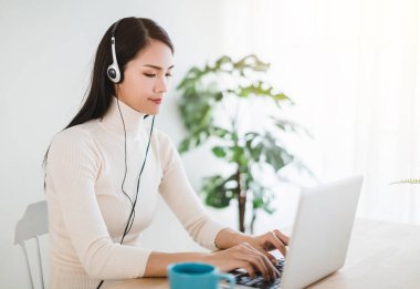 Dizüstü bilgisayarda çalışan ve evdeki oturma odasında video kullanan genç bir kadın.