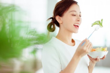 Genç mutlu kadın evde sağlıklı salata yiyor.