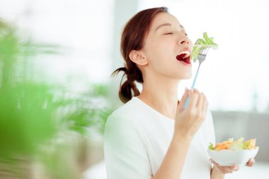 Genç mutlu kadın evde sağlıklı salata yiyor.