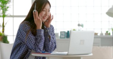 Genç kadın kulaklık takıyor ve evdeki dizüstü bilgisayarda video konferansı yapıyor.